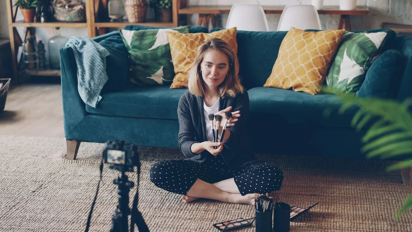 A course creator filming a makeup lesson on a camera set up in her living room