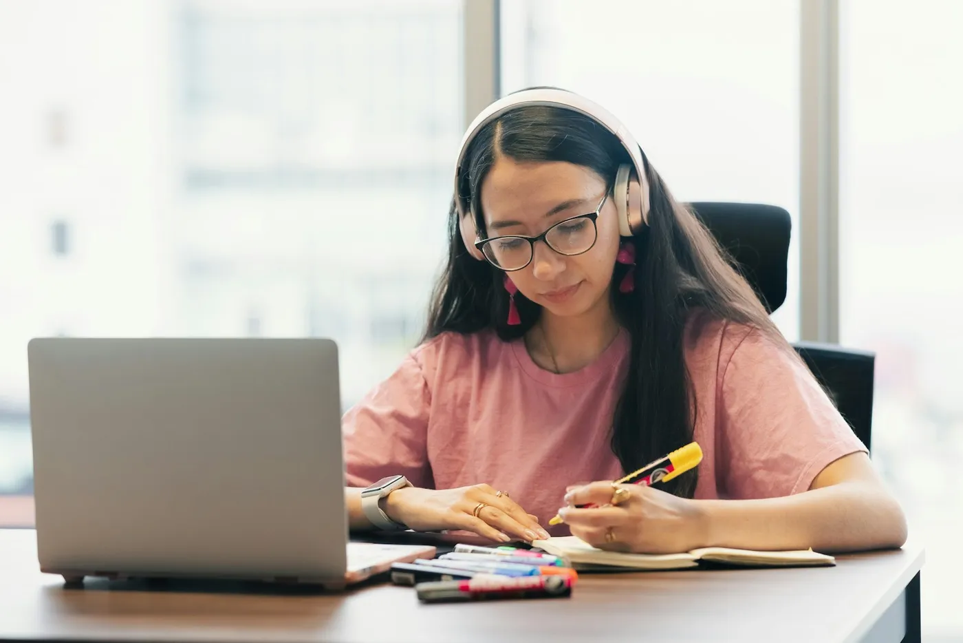 A student in headphones working through an online course on a laptop and taking notes